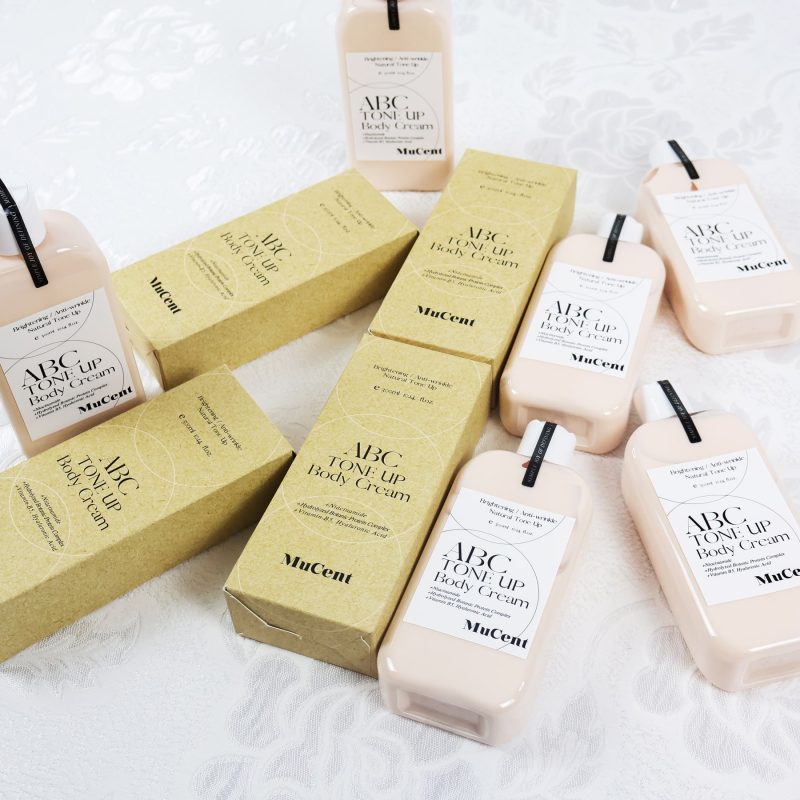 MuCent ABC Tone Up Body Cream bottles photographed in a creative still life arrangement