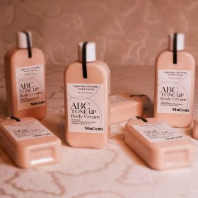 MuCent ABC Tone Up Body Cream bottles arranged on a light floral textured background.